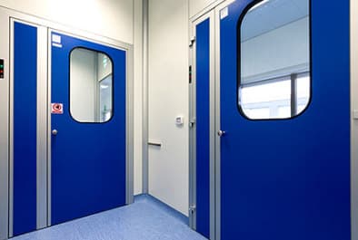 Blue cleanroom doors with vision panels and interlocked airlock arrangement.