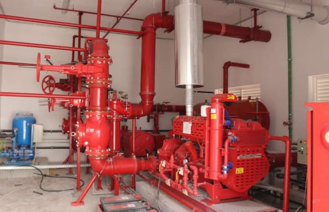A red fire-safety pump skid with valves and pipework in a plant room.